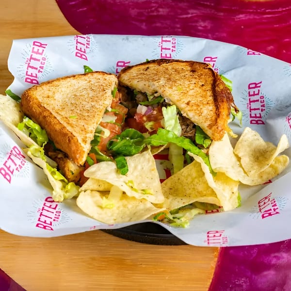 A grilled sandwich from The Better Taco, filled with meat, lettuce, and pico de gallo, served with tortilla chips.