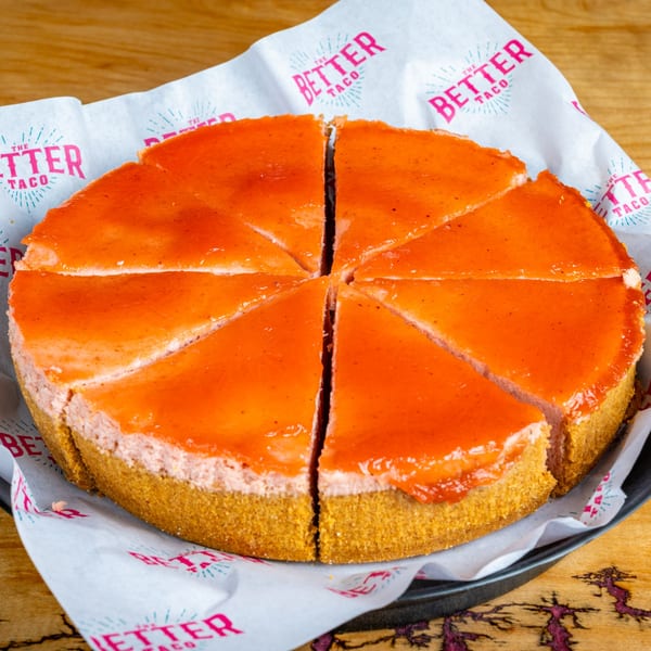 A whole strawberry cheesecake, sliced into eight pieces, on The Better Taco branded paper.