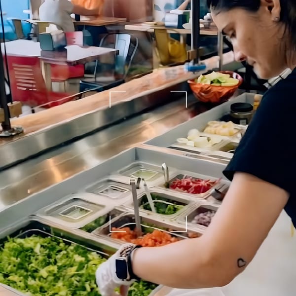 A Better Taco employee prepares food at a counter with various fresh toppings in containers.