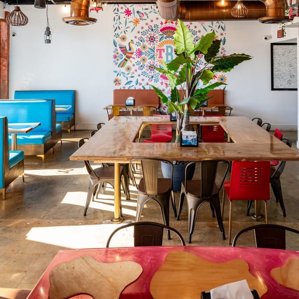 The Better Taco restaurant interior with blue booths, a large communal table, and a colorful floral mural.
