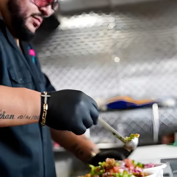 Chef in black gloves and pink glasses preparing a taco with fresh ingredients at The Better Taco.