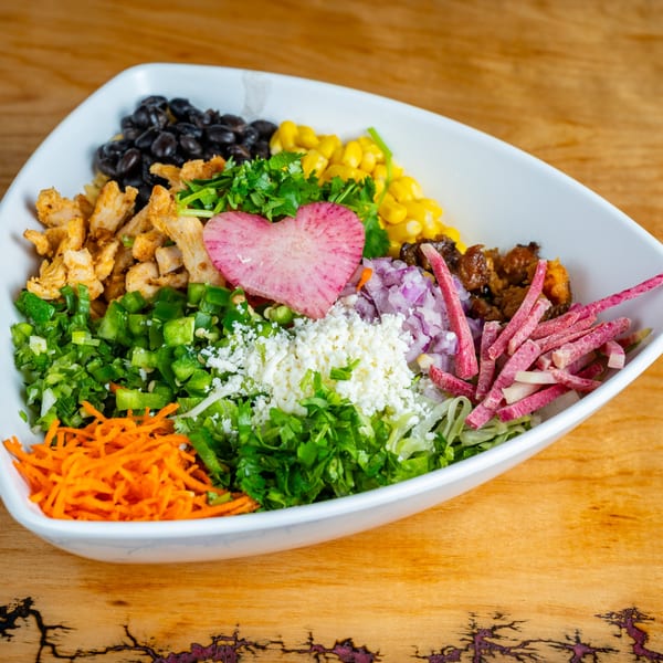 A colorful Mexican bowl with chicken, black beans, corn, vegetables, and a heart-shaped radish.